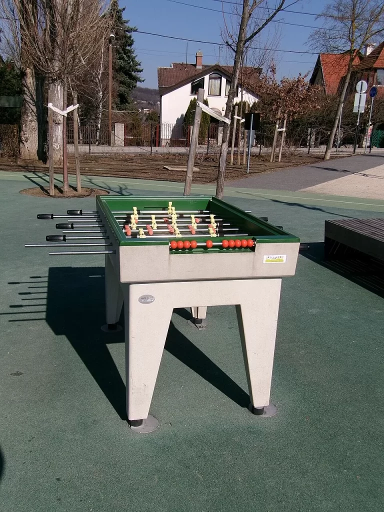 Un baby-foot d'extérieur installé dans un parc, sous le soleil.